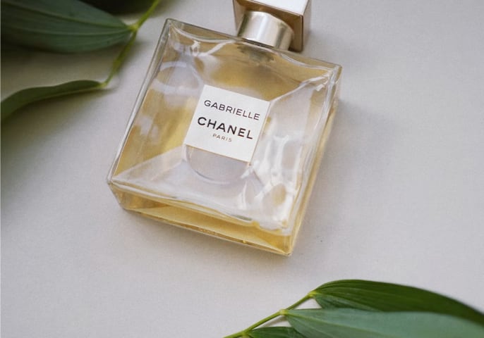 A bottle of Gabrielle Essence Eau De Parfum, surrounded by plants.